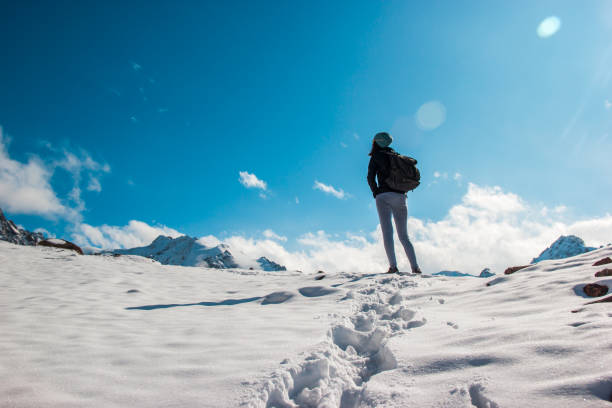 istock A young woman on a snow top amid a blue sky. White clouds. 1202312484