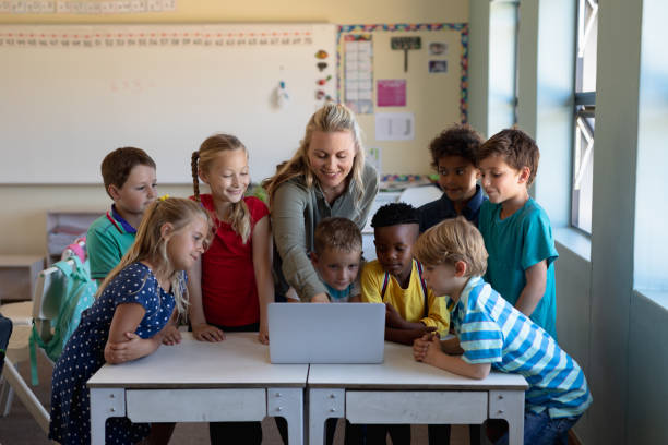 istock Female teacher using a laptop computer with group of schoolchildren 1202313735