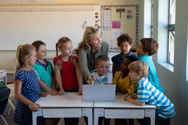 istock Female teacher using a laptop computer with of schoolchildren 1202313788