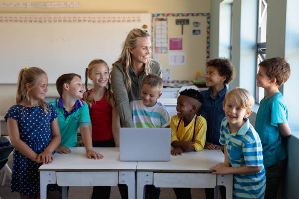 istock Female teacher using a laptop computer with of schoolchildren 1202313794