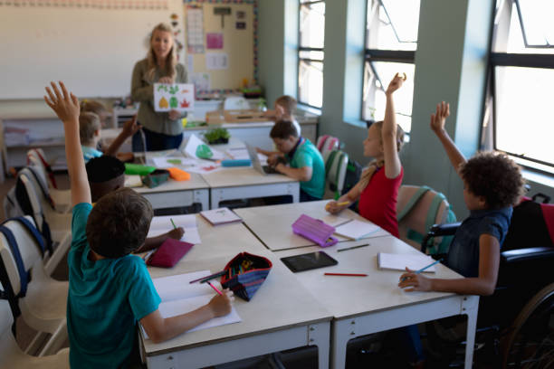 istock Group of schoolchildren raising their hands in an elementary school classroom 1202314018