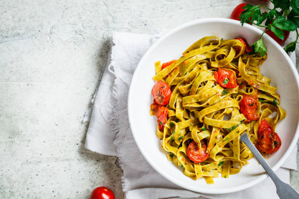 Green spinach pasta with tomatoes and herbs, top view. Healthy vegan food concept. Green spinach pasta with tomatoes and parsley. Healthy vegan food concept. spinach pasta stock pictures, royalty-free photos & images