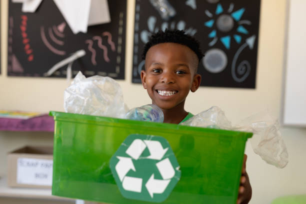 écolier retenant une caisse verte avec un logo blanc de recyclage là-dessus - african descent africa african culture classroom photos et images de collection