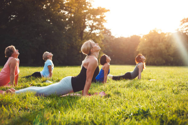 istock Mixed age group of people practicing yoga outside in the park while sunset 1202315785