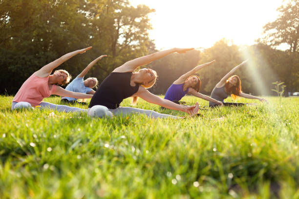 istock Mixed age group of people practicing yoga outside in the park while sunset 1202316537