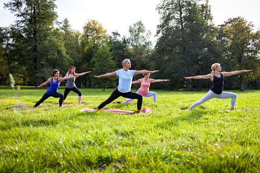 Mixed age group of people practicing yoga outside in the park