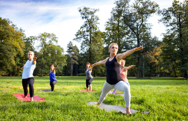 istruttore che esegue esercizi di yoga con fascia d'età mista di persone all'esterno nel parco - yoga exercising outdoors group of people foto e immagini stock