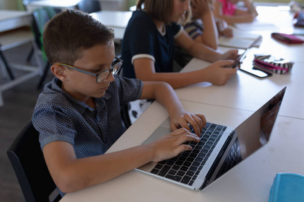 istock Schoolboy wearing glasses sitting at a desk using a laptop computer 1202320032