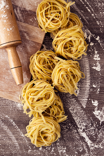 Tagliatelle pasta background with rolling pin and flours on brown table