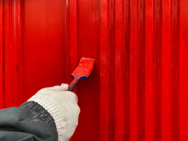 istock A man paints a wall outdoors with a red paint brush, a brush in his hand in a white protective glove,  renovation concept 1202324243