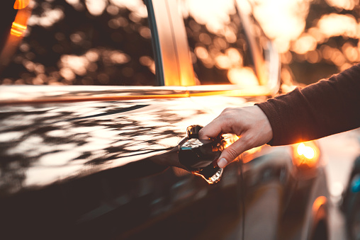 Hand on handle. Close-up of woman hand opening a car door with sunlight effect.