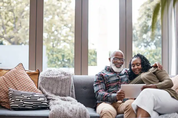 Shot of a mature couple using a digital tablet while relaxing together on a sofa at home