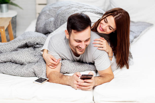 istock Young couple laying in bed with mobile phone on hand 1202336368