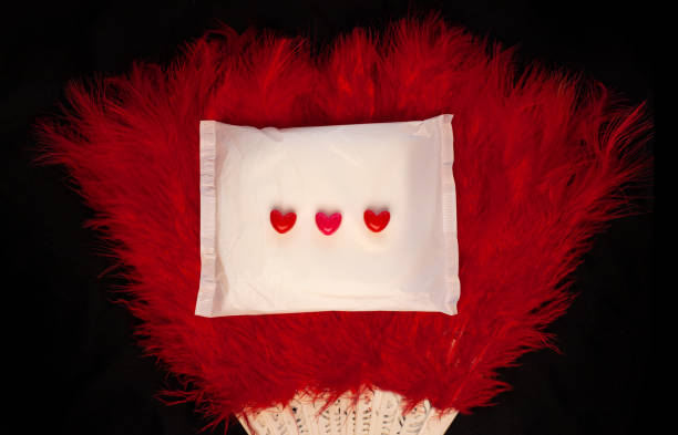 istock Irregular period concept. Menstrual cycle pad with feathers fan red hearts on black background. Menorrhagia menstruation 1202338314