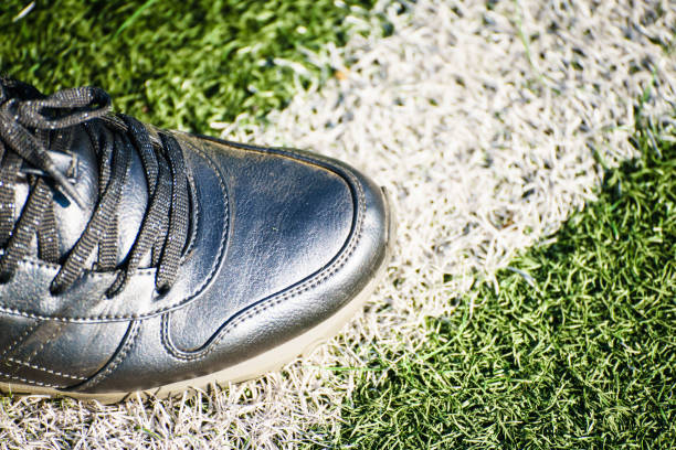 From above shot of foot standing on white line on green soccer field.