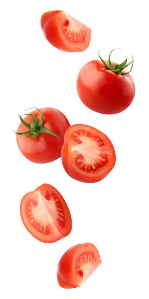 falling tomatoes isolated on a white background with a clipping path. whole red tomatoes and cut pieces fly in the air. vegetables fall down.