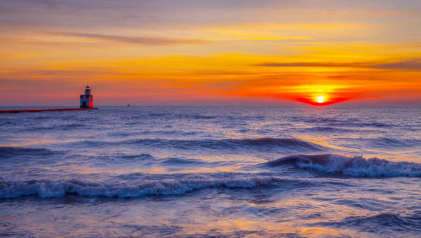 Red sunrise with lighthouse over cold Lake Michigan with big waves in December.  The Lake is usually frozen at this time of year, but climate change has kept the lake liquid this winter.