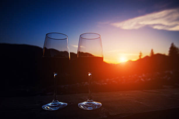 istock Two glasses of wine at sunset dramatic sky on mountain landscape background 1202342209