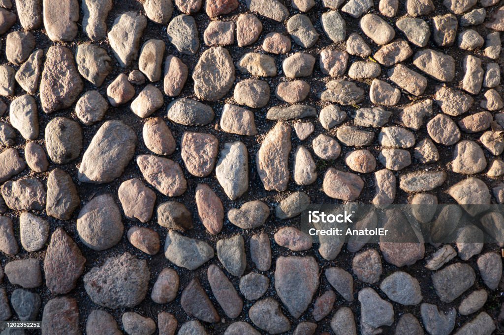 Vintage pavement made of small cobblestones of gray granite. Part of the space is lit by the sun, another part is in the shade. Background. Texture. Abstract Stock Photo