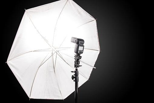 Studio stand with speedlight photo flash and white umbrella reflector, equipment in a photo studio.