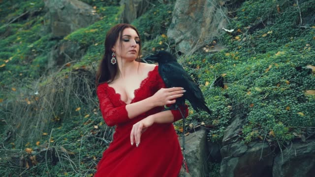 nymph with raven on hand. Woman in red dress with deep necklinen stroking bird