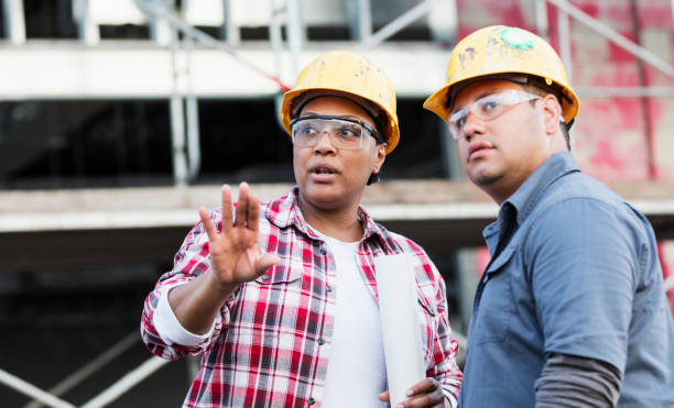 dois trabalhadores falando em um canteiro de obras, olhando - construction worker construction building contractor hardhat - fotografias e filmes do acervo