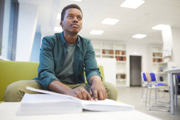 Blind Student in College Portrait of young African-American man reading braille while studying in school library, copy space blindness stock pictures, royalty-free photos & images