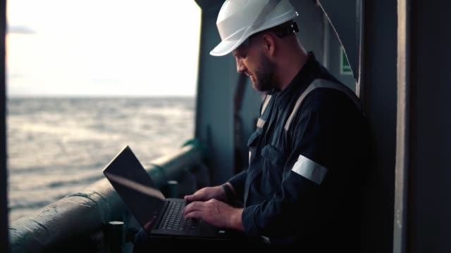 Marine chief officer or captain on deck of vessel or ship watching laptop