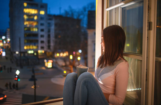 istock Young Woman Enjoying Tranquil Evening and Tea on Window Sill 1202391266