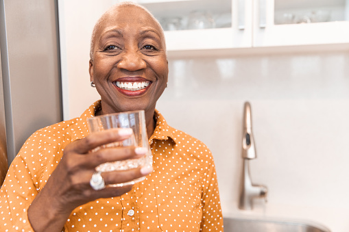 Senior African decent woman with a glass of water in the kitchen