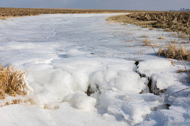 campo agrícola inundado após tempestades de chuva de inverno com água virando gelo à medida que a temperatura caía abaixo de zero. - storm corn rain field - fotografias e filmes do acervo