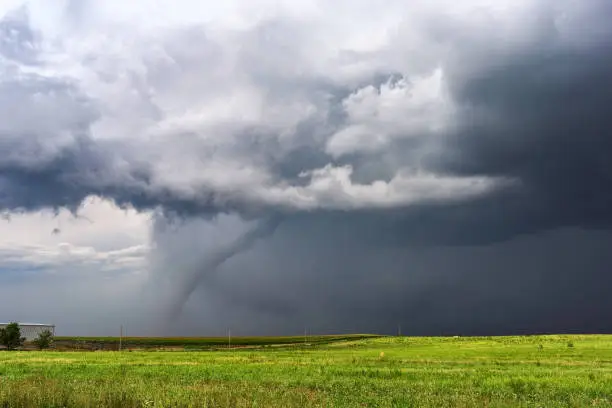 Tornado and dark storm clouds beneath a supercell thunderstorm over a field in Colorado.