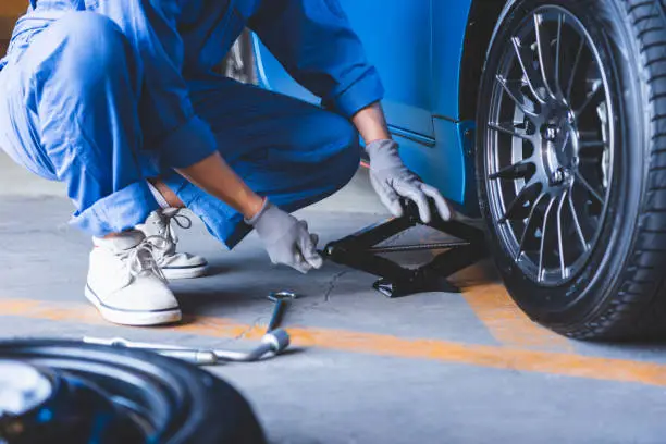 Photo of Car mechanics changing tire at auto repair shop garage. Transportation and Business working people concept. Automobile technician maintenance vehicle by customer claim order. Wheel repair service