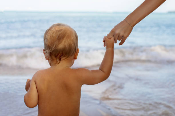 istock Little kid holding hands with faceless mom in beach 1202419974