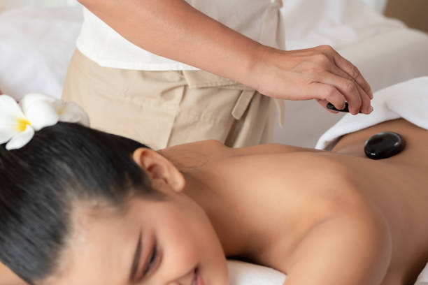 jeune femme asiatique se trouvant se reposant obtenant le massage chaud de pierre dans le salon de spa. concept de traitement de beauté. sélectionnez la main de mise au point de masseuse - massaging spa treatment stone massage therapist photos et images de collection