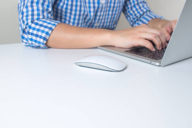 白い机の上にラップトップコンピュータの上を使用して、青いチェック柄のシャツを着た男の手のクローズアップ。 - shirt close up white button ストックフォトと画像