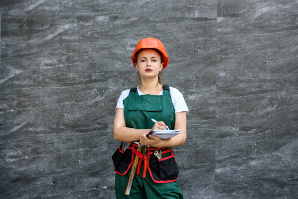 istock Woman worker in coverall with tool belt posing near grey wall 1202440598
