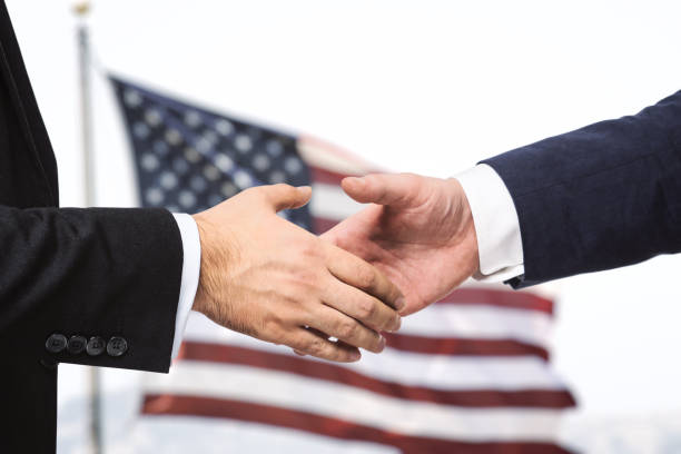 istock Two businessmen shake hands on a US flag backgrond, closeup 1202440877