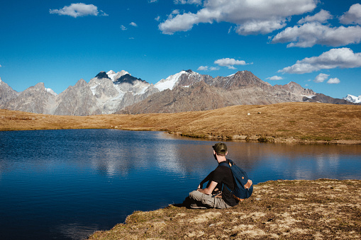 a young man sits on the edge of a lake and looks at the Caucasus Mountains in Georgia in the fall