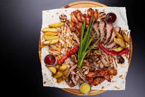 istock Assorted delicious grilled meat with vegetable. Mixed grilled bbq meat with vegetables. Mixed grilled meat on wooden platter. Top view. 1202443848