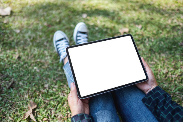 a woman holding and using black tablet pc with blank white desktop screen while sitting in the outdoors