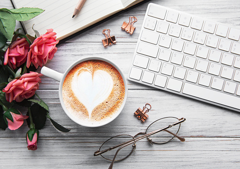 Composition Valentine's Day. Female desktop Ñomputer keyboard, Ñup of coffee with  heart pattern on white wooden background. Valentine day concept, top view, flat lay.