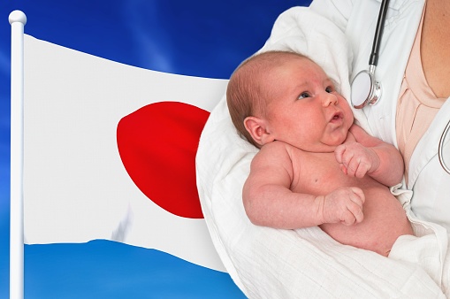 Birth rate in Japan. Newborn baby in hands of doctor on national flag background.