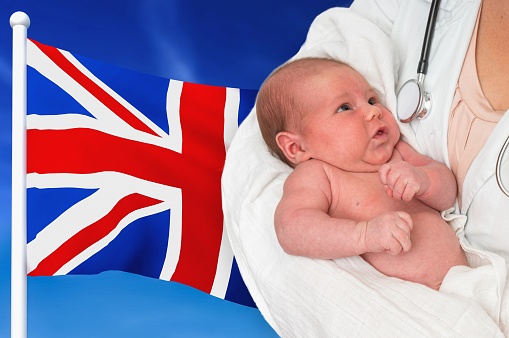 Birth rate in United Kingdom. Newborn baby in hands of doctor on national flag background.