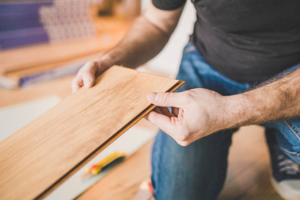An Experienced Carpenter is Feeling Tired and Exhausted so He is Taking a Break and Relaxing While Leaning on a Work Table in a Spacious Workshop.