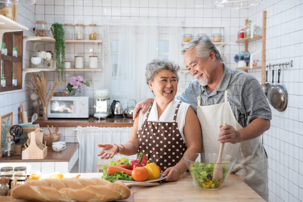 coppia anziana che si diverte in cucina con cibo sano - pensionati che cucinano il pasto a casa con uomo e donna che preparano il pranzo con verdure biologiche - concetto di anziani felici con pensionato maturo divertente. - 60s senior adult breakfast cheerful foto e immagini stock