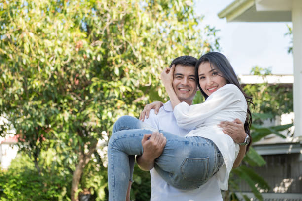 Young loving couple have fun in park Young loving couple have fun in park. Boyfriend carry on his asian girlfriend in arms in front yard of house. mum new boyfriend stock pictures, royalty-free photos & images