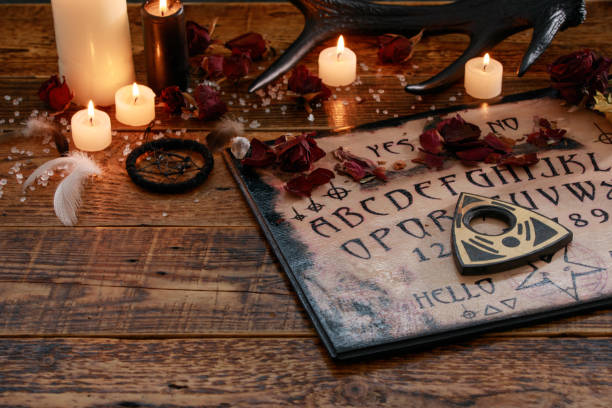 istock Mystic ritual with Ouija and candles. Devil's board concept, black magic or fortune telling rite with occult and esoteric symbols. 1202461307