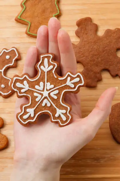 Gingerbread snowflake cookie decorated with white icing on female hand. Hand holding cookie