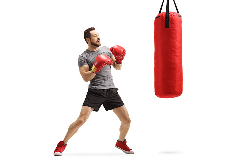 Full length shot of a young man exercising box with a red punching bag isolated on white background